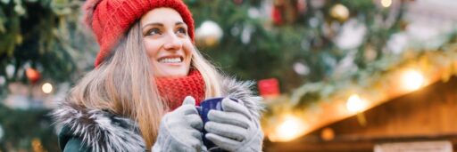 Winters uitje : Een dame met een muts op in de winter voor een kerstboom met een beker warme chocolademelk